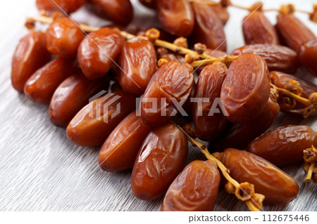 Sweet dried dates on a branch on a kitchen board. Oriental treats. Healthy nutritious snack. Sweet dried dates on a branch on a kitchen board. Oriental treats. Healthy nutritious snack. 112675446