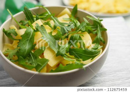 Uncooked sliced potatoes with green herb arugula close up. Cooking traditional dishes Uncooked sliced potatoes with green herb arugula close up. Cooking traditional dishes 112675459