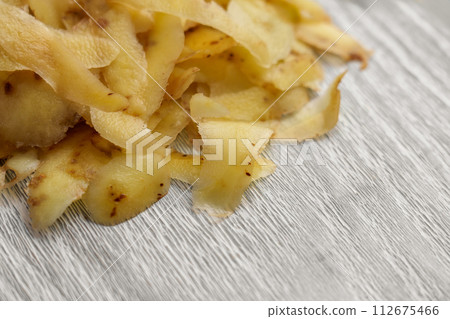 Pile of fresh potato peelings. Kitchen garbage on a wooden cutting board close up Pile of fresh potato peelings. Kitchen garbage on a wooden cutting board close up 112675466