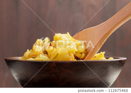 Fried steaming hot potatoes in a rustic bowl with a wooden spoon on a brown background close up. Traditional cuisine Fried steaming hot potatoes in a rustic bowl with a wooden spoon on a brown background close up. Traditional cuisine 112675468
