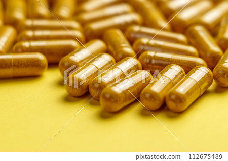 Yellow turmeric (curcuma) supplement capsules on a creative colour background. Herbal medicine pills with curcumin powder. Yellow turmeric (curcuma) supplement capsules on a creative colour background. Herbal medicine pills with curcumin powder. 112675489