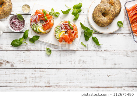 Salmon sandwiches with bagel, salted fish, fresh cucmber, onion and basil on white background, top view. Healthy breakfast with salmon toasts 112675490