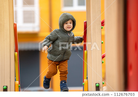 Cute happy toddler boy three years old is playing on the playground in a residential complex. Healthy spring activity for children. Children's games. Cute happy toddler boy three years old is playing on the playground in a residential complex. Healthy spring activity for children. Children's games. 112676703