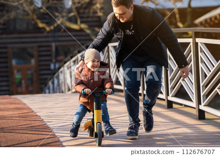 Happy father and son ride a bicycle on a bridge on a sunny day. Having fun together with family. Spending time Happy father and son ride a bicycle on a bridge on a sunny day. Having fun together with family. Spending time 112676707