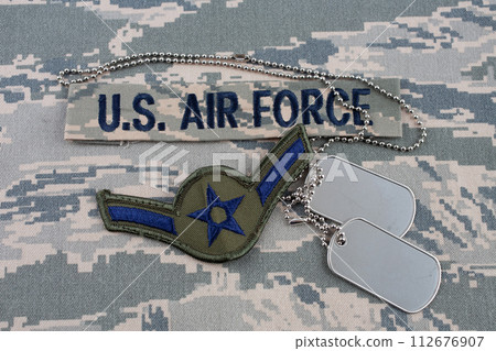 US AIR FORCE branch tape and Airman rank patch and dog tags on digital tiger-stripe pattern Airman Battle Uniform (ABU) background US AIR FORCE branch tape and Airman rank patch and dog tags on digital tiger-stripe pattern Airman Battle Uniform (ABU) background 112676907