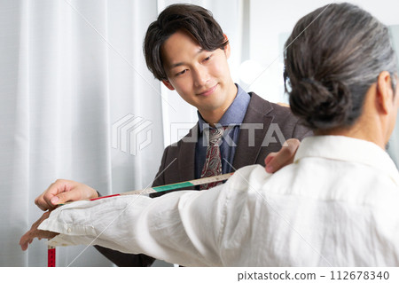 A suit shop clerk taking measurements 112678340