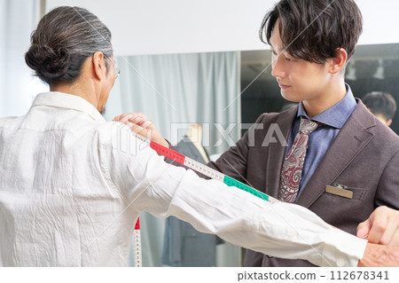 A suit shop clerk taking measurements A suit shop clerk taking measurements 112678341