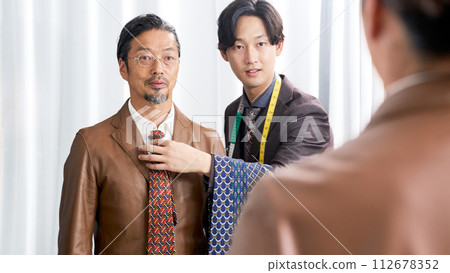 年輕男造型師在鏡子前看著顧客的領帶 112678352