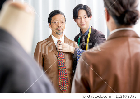 Men's personal stylist looking at customer's tie in front of the mirror Men's personal stylist looking at customer's tie in front of the mirror 112678353