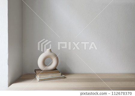 Elegant neutral still life with modern ceramic vase on old books. Wooden table, desk. White wall background. Empty copyspace, no people. Scandinavian, boho home decor. Living room. 112678370
