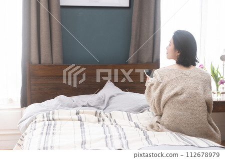 Young woman sitting on bed Young woman sitting on bed 112678979