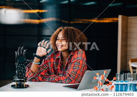 Portrait of a Black teenage student learning about a robotic arm in a classroom. She controls the arm for her engineering project showcasing intelligence and embracing technology. 112679403