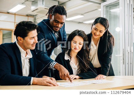 A global team, with a female leader, collaborates in a meeting room. Their teamwork is evident as they discuss financial results, share ideas, and brainstorm strategies for success. A global team, with a female leader, collaborates in a meeting room. Their teamwork is evident as they discuss financial results, share ideas, and brainstorm strategies for success. 112679404