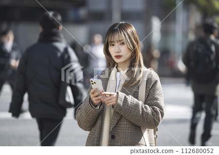 一名 20 多歲的女性拿著智慧型手機看著相機 一名 20 多歲的女性拿著智慧型手機看著相機 112680052