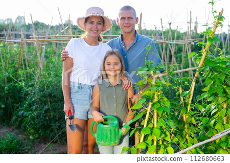 Portrait of daughter and parents with watering cans in summer garden Portrait of daughter and parents with watering cans in summer garden 112680663