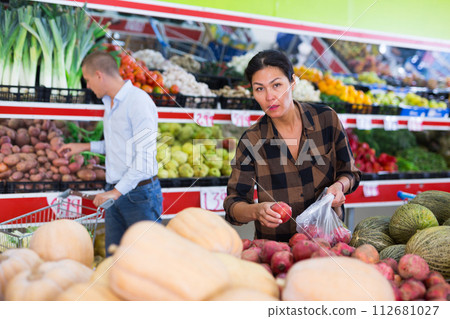 Asian woman choosing pomegranates on counter in greengrocery 112681027