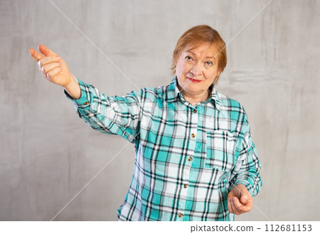 Smiling senior woman in plaid shirt gesturing towards with hand Smiling senior woman in plaid shirt gesturing towards with hand 112681153