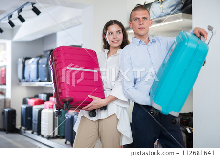 Portrait of a young male and girl in a shop, holding travel suitcases 112681641