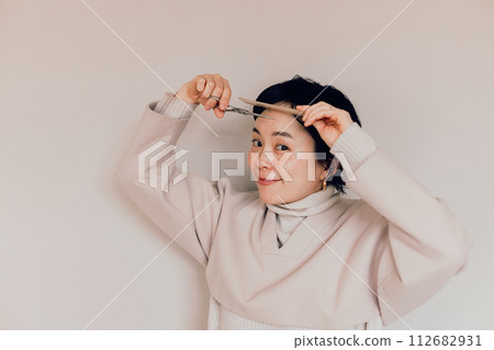 Stylish woman with a short haircut doing her own haircut Stylish woman with a short haircut doing her own haircut 112682931