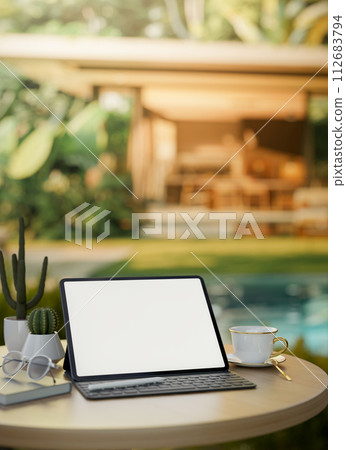 A digital tablet mockup on a table by the pool in a beautiful outdoor garden of a home villa. A digital tablet mockup on a table by the pool in a beautiful outdoor garden of a home villa. 112683794