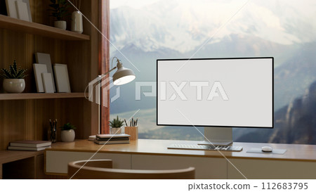 A home office features a computer mockup against the window with a view of snow-capped mountains. A home office features a computer mockup against the window with a view of snow-capped mountains. 112683795