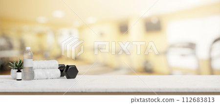 A presentation space on a white table features a dumbbell, towels, and a water bottle in a fitness. 112683813