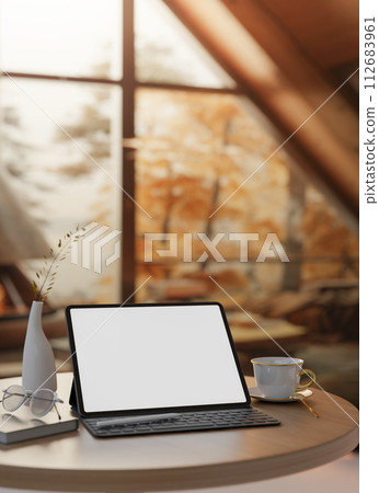 A close-up image of a white-screen digital tablet mockup on a wooden table in a cozy autumn cabin. A close-up image of a white-screen digital tablet mockup on a wooden table in a cozy autumn cabin. 112683961
