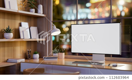 A contemporary office features a computer on a table against the window with a nighttime city view. A contemporary office features a computer on a table against the window with a nighttime city view. 112683964