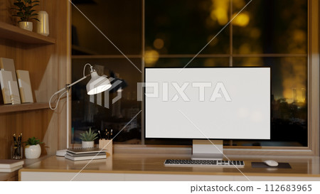 A contemporary office with a computer mockup on a wooden desk against the window with a night view. 112683965