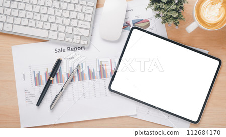 Workspace with sales report, digital tablet, keyboard, and cup of coffee on wooden desk. 112684170