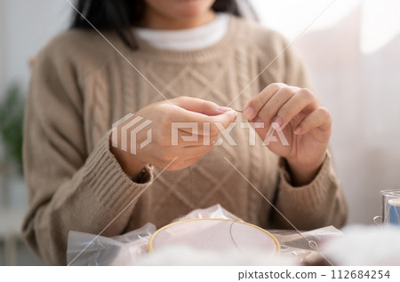 A close-up image of a woman inserting a needle, threading a sewing needle, sewing at home. 112684254
