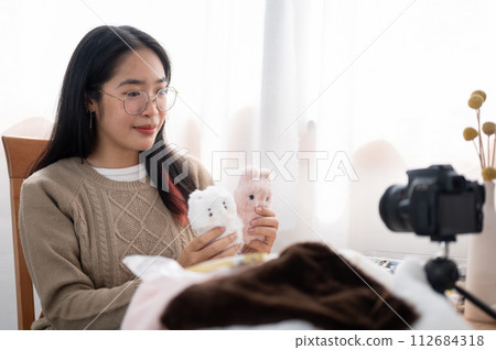 A cheerful young Asian female content creator showing her cute handmade plushie to the camera. 112684318