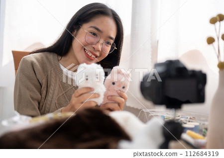 A cheerful young Asian female content creator showing her cute handmade plushie to the camera. 112684319