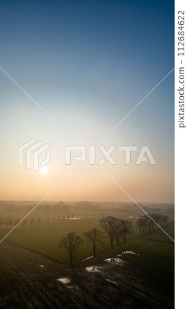 Gentle Sunrise Over a Misty Agricultural Landscape 112684622