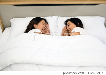 Two young Asian couple women lying Sharing a Joyful Moment in Bed 112685914