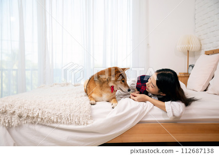 Asian young woman lying with brown Shiba Inu Enjoying a Tender Moment on bed 112687138