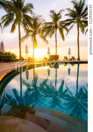 Umbrella and chair around swimming pool in hotel resort with sunrise in morning 112689185
