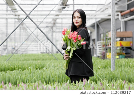 Young woman standing in large greenhouse and holding a blooming tulips in her hands 112689217