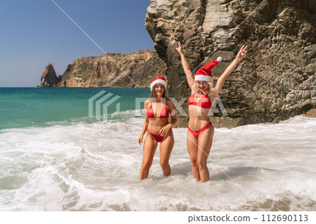 Women in Santa Claus hats run into the sea dressed in red swimsuits. Celebrating the New Year in a hot country Women in Santa Claus hats run into the sea dressed in red swimsuits. Celebrating the New Year in a hot country 112690113