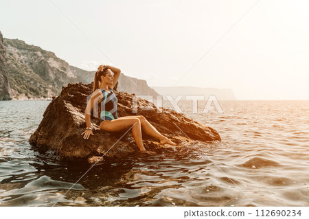 Woman travel summer sea. A happy tourist in a blue bikini enjoying the scenic view of the sea and volcanic mountains while taking pictures to capture the memories of her travel adventure. 112690234