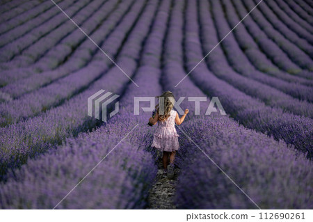 Lavender field girl. Back view happy girl in pink dress with flowing hair runs through a lilac field of lavender. Aromatherapy travel 112690261