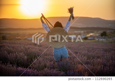 Woman lavender field sunset. Back view woman in a white blouse, denim shorts and hat. Aromatherapy concept, lavender oil, photo session in lavender 112690265