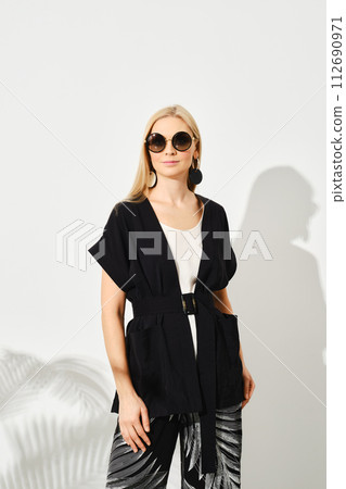 Woman wearing black outer garment paired with a white top and patterned pants 112690971