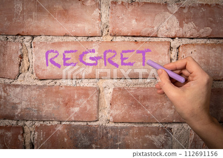 REGRET. Text written with purple chalk on a red brick background 112691156