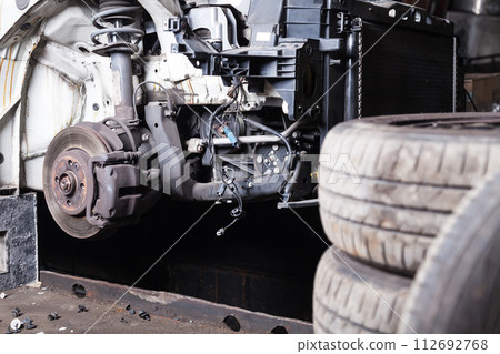 The front part of the car after an accident in a car repair service with a disassembled hood and metal grille and various parts in the garage box. The front part of the car after an accident in a car repair service with a disassembled hood and metal grille and various parts in the garage box. 112692768