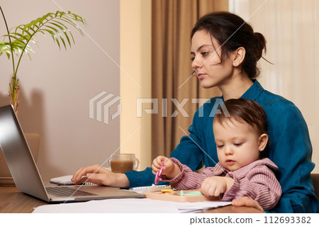 beautiful businesswoman working on laptop with her little child girl at home beautiful businesswoman working on laptop with her little child girl at home 112693382