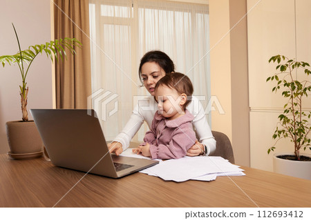 Cheerful pretty businesswoman working at home with her little child girl 112693412