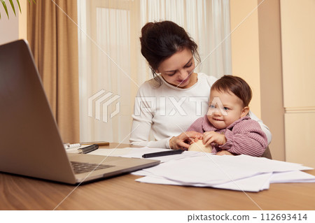 Cheerful pretty businesswoman working at home with her little child girl Cheerful pretty businesswoman working at home with her little child girl 112693414