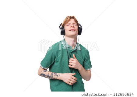 a young man with red hair dressed in a green t-shirt in large headphones dances and enjoys a young man with red hair dressed in a green t-shirt in large headphones dances and enjoys 112693684