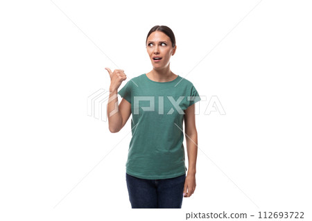 young brunette woman in a t-shirt points with her hand to the side on an empty space 112693722